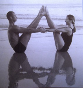 A couple doing the boat pose on the beach